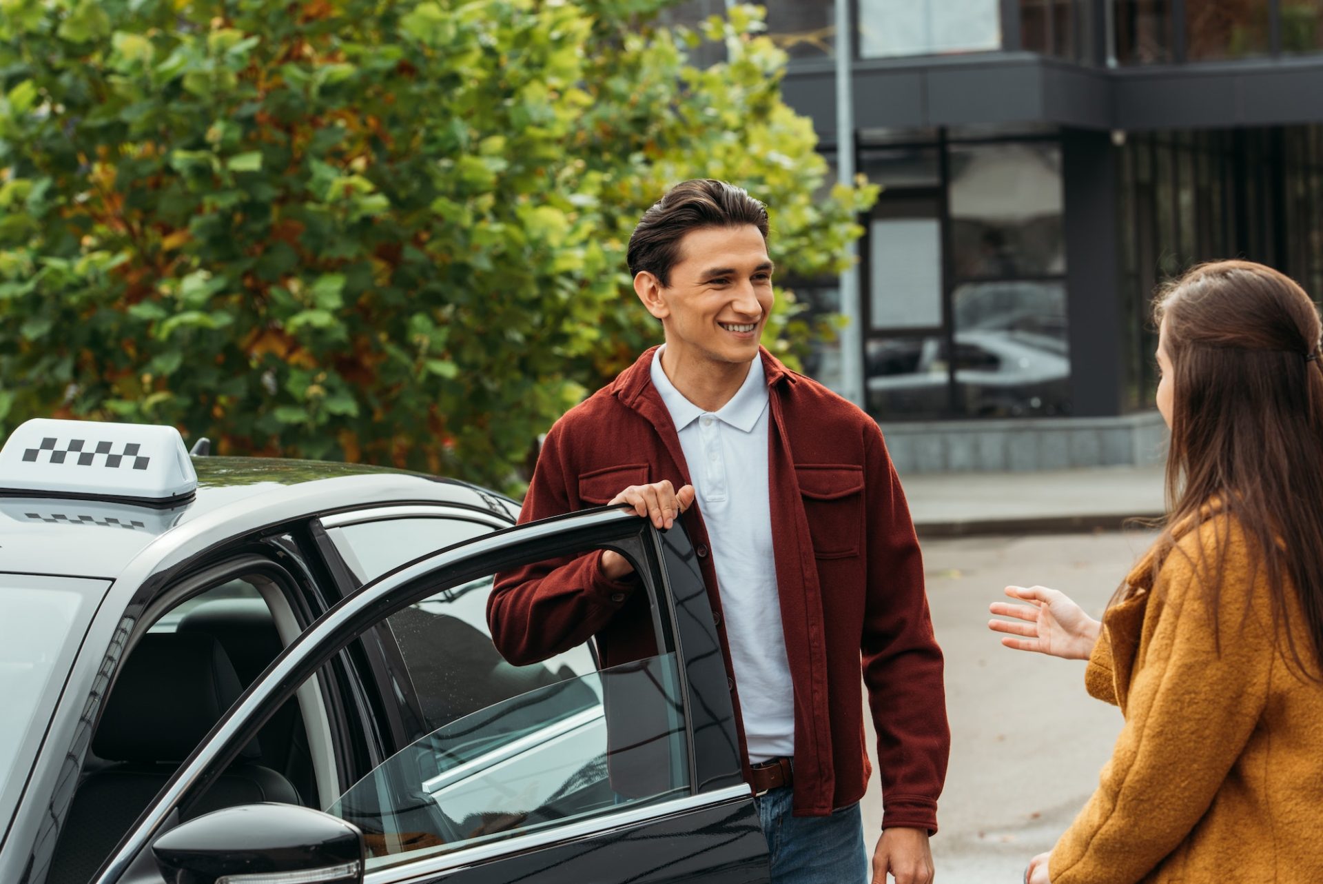 Woman talking with smiling taxi driver beside car